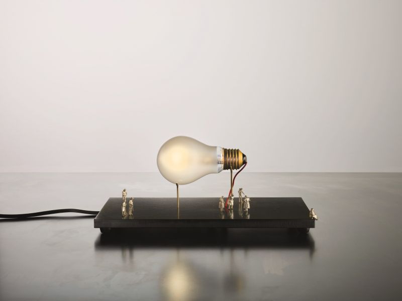 I Ricchi Poveri Tischleuchte: Glühbirne auf Sockel mit kleinen Figuren. Designlampe von Ingo Maurer.